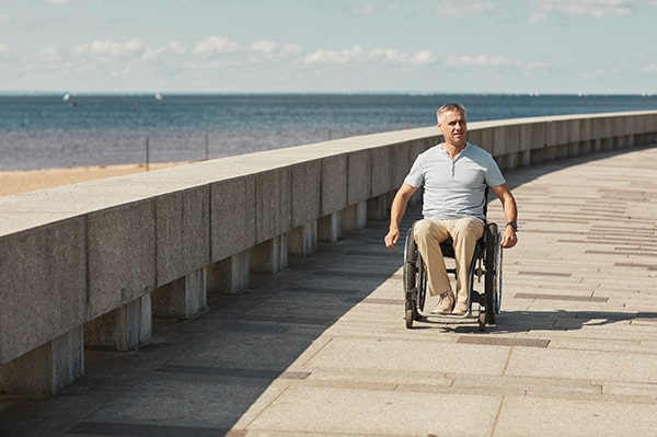 Person im Rollstuhl am Meer auf Promenade