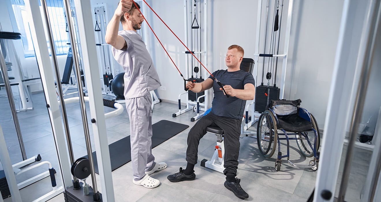 Person in der Reha-Phase sitzt in einem Rollstuhl in einem hellen Therapiebereich